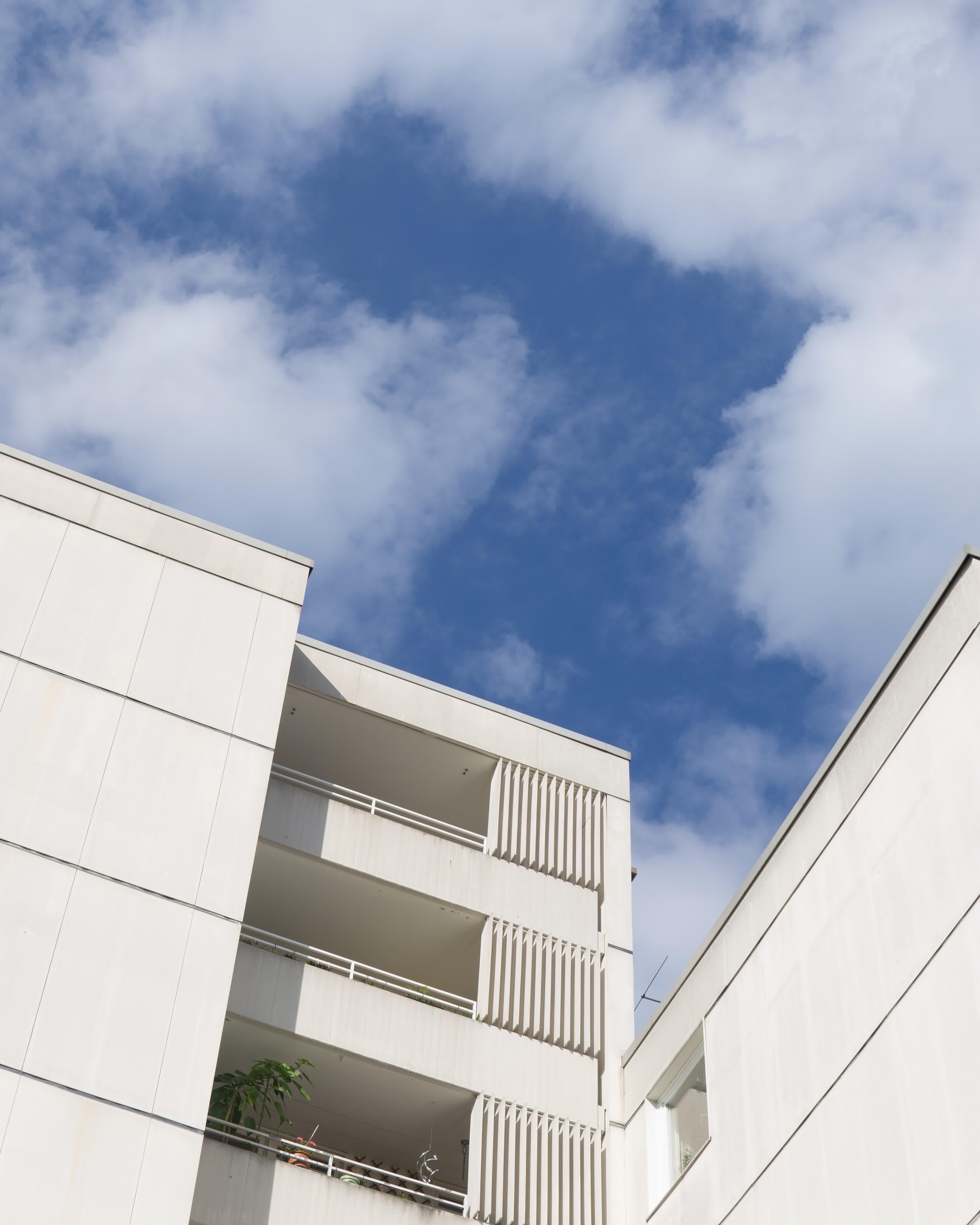 Weißes Mehrfamilienhaus mit blauem, leicht bewölktem Himmel, von unten fotografiert